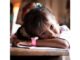 A young girl resting her head on a table, looking thoughtful.