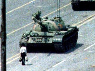 Man standing defiantly in front of a tank on a city street.