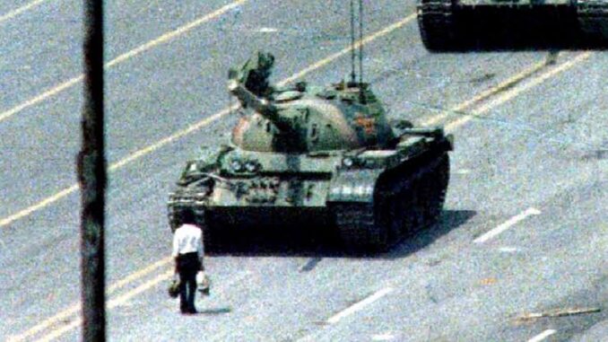 Man standing defiantly in front of a tank on a city street.