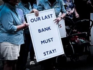 Protesters hold a sign saying 'OUR LAST BANK MUST STAY!'.