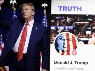 Donald Trump standing near a campaign poster with American flags.