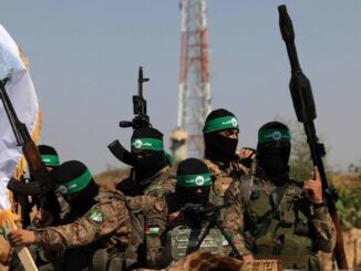 Armed militants in camouflage with green headbands raising weapons.