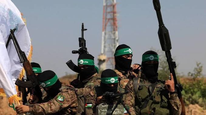 Armed militants in camouflage with green headbands raising weapons.