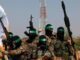 Armed militants in camouflage with green headbands raising weapons.