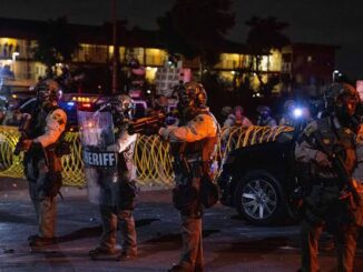 Sheriff deputies in tactical gear stand alert at night during a security operation.