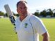 Cricketer holding a bat, ready to play on a sunny day.