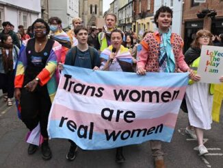 People holding a banner saying 'Trans women are real women' at a march.