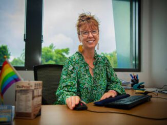 Smiling woman in green blouse working at her desk by a window.