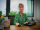 Smiling woman in green blouse working at her desk by a window.