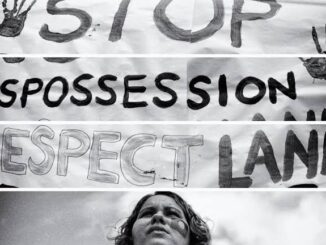 A person stands in front of a protest sign demanding respect for land and stopping dispossession.