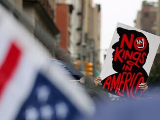 Protest sign reading 'New King is America' with American flags in the foreground.