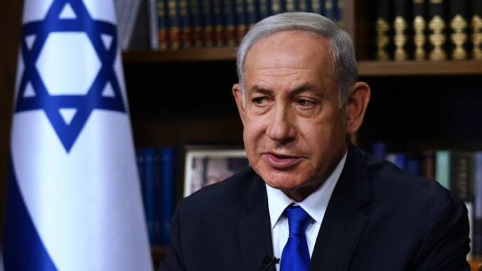 Portrait of a serious man in a suit with an Israeli flag in the background.