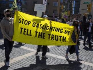 Protesters hold a yellow banner demanding truth about gaslighting.