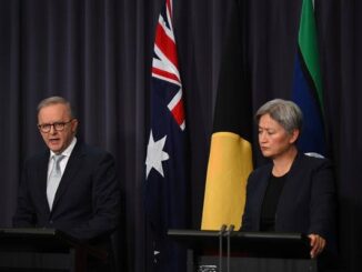 Two officials speak at a podium with Australian and Aboriginal flags behind them.