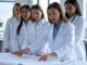 A group of female scientists in white lab coats reviewing documents.