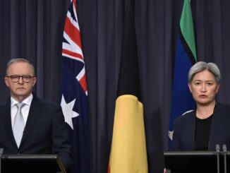 Two individuals seated at a table with Australian and Aboriginal flags in the background.