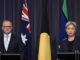 Two individuals seated at a table with Australian and Aboriginal flags in the background.