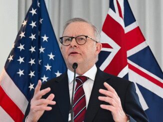 A man speaking at a podium with US and Australian flags behind him.
