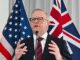 A man speaking at a podium with US and Australian flags behind him.