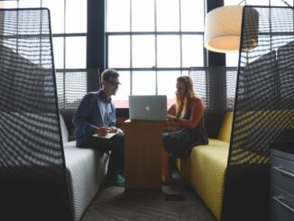Two colleagues discussing work on a laptop in a modern office lounge.