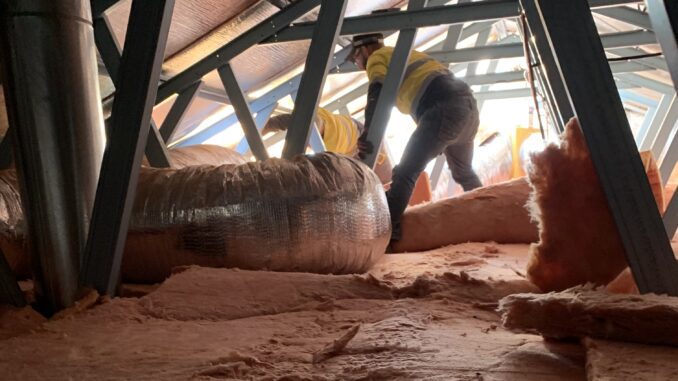 Person installing insulation in an attic space.