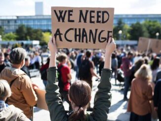 Person holds a sign reading 'We Need A Change' at a public protest.