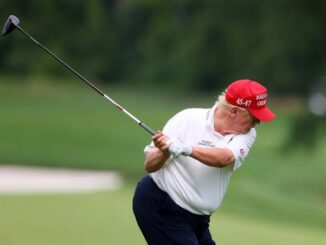 Man in red cap swinging golf club on green course.