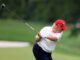 Man in red cap swinging golf club on green course.