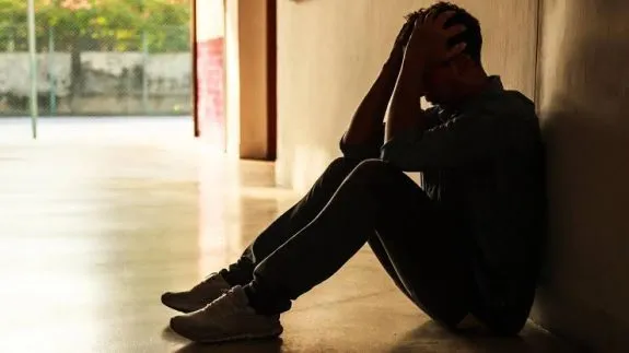 Person sitting against wall, holding head, distressed.