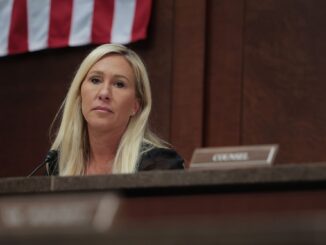 Woman seated in courtroom with flag background.