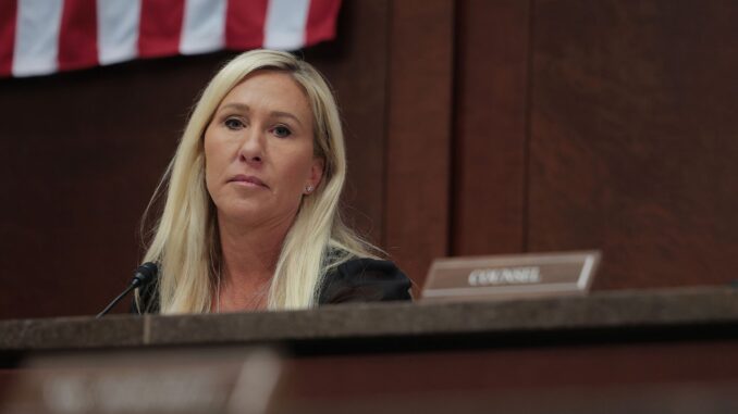 Woman seated in courtroom with flag background.