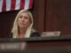 Woman seated in courtroom with flag background.
