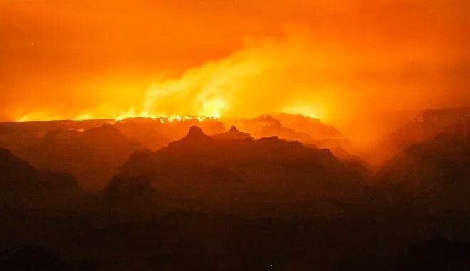 Orange sky over silhouetted mountainous landscape.