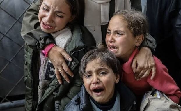 Three children crying, embraced by an adult.