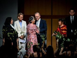 Group of people on stage with foliage.