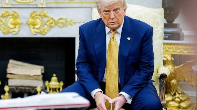 Man seated in ornate room, looking serious.