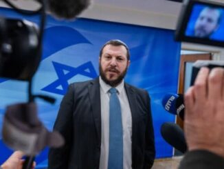 Man speaking to media with Israeli flag backdrop.