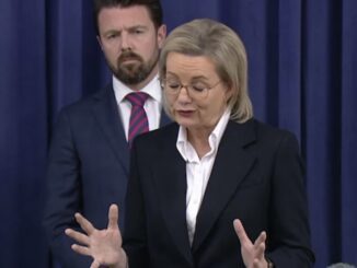 Woman speaking at a press conference, man listening.