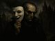 Man holding mask in dark, eerie setting.