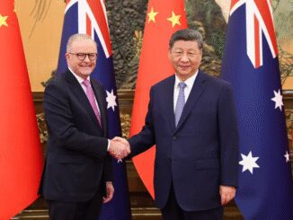Two leaders shaking hands with flags behind.