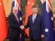 Two leaders shaking hands with flags behind.
