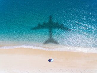 Shadow of an airplane over a beach with a person under an umbrella.