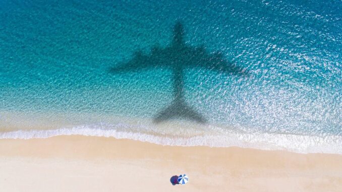 Shadow of an airplane over a beach with a person under an umbrella.