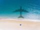 Shadow of an airplane over a beach with a person under an umbrella.