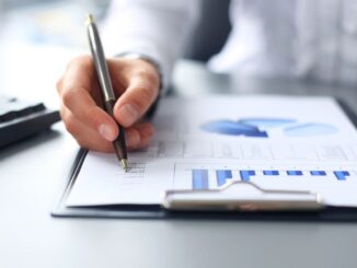 Person writing on financial report with charts.