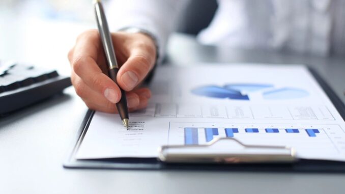 Person writing on financial report with charts. Person writing on financial report with charts.
