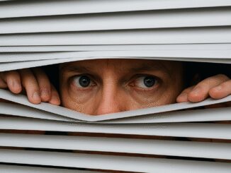 Person peeking through partially opened window blinds.