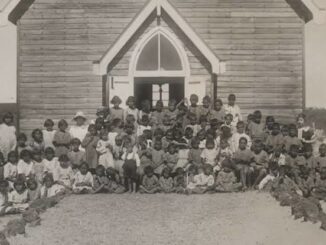 Large group of children outside wooden building.