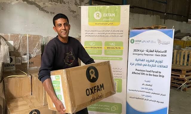 Man holding Oxfam food parcel, smiling.