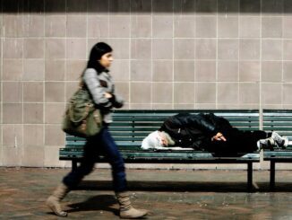 Woman walks past person sleeping on bench.